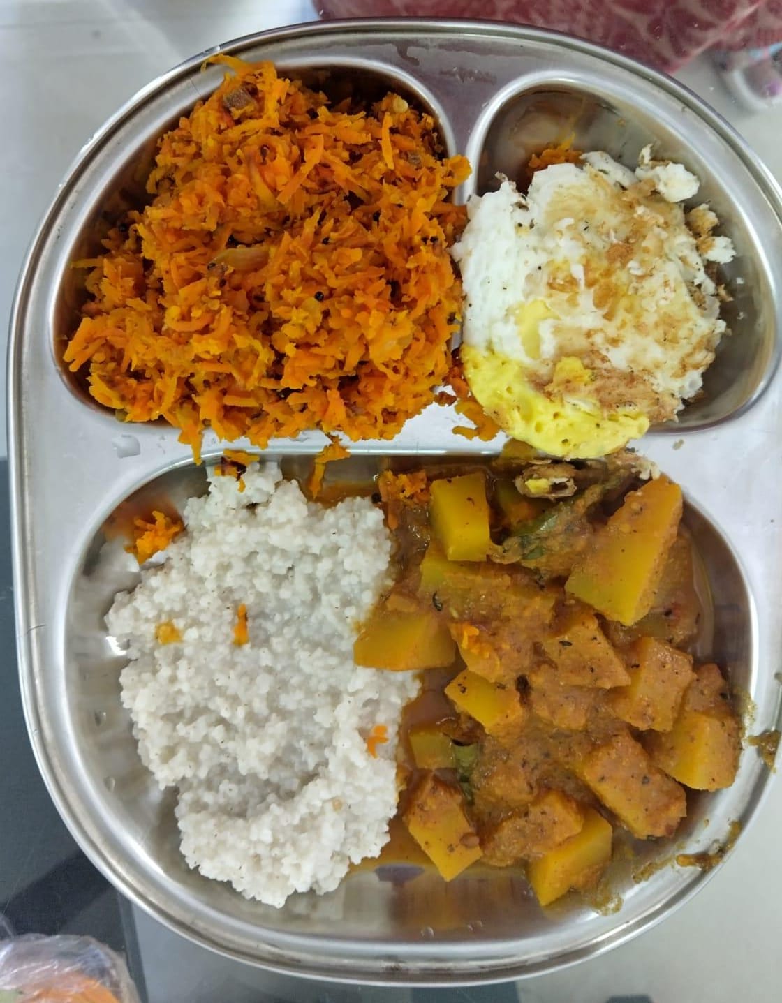 Dr. Anitha's balanced meal plate with carrot poriyal, a fried egg, little millet, and a vegetable curry in a steel partition plate