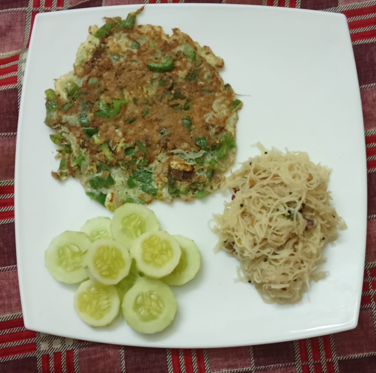 A plate of a vegetable egg dish with capsicum, vermicelli, and cucumber slices
